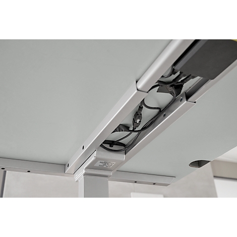 Close-up of the underside of a desk with cable management. Gray table top with integrated cable tray, cables and power supply.