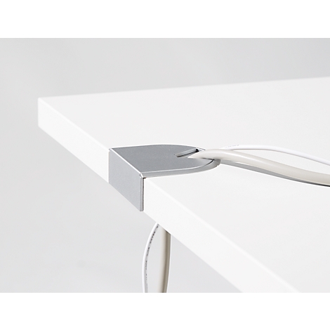 Corner of a white desk with a metal cable grommet. White cables run through it.