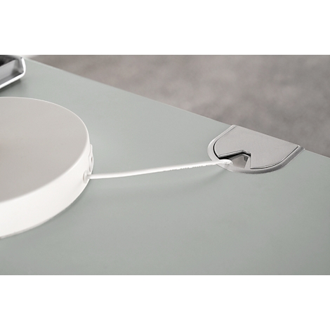 Close-up of a grey desk with a white cable and a cable grommet.