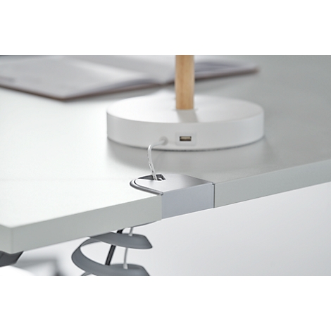 Detail of a tabletop with integrated cable holder, above a desk lamp.