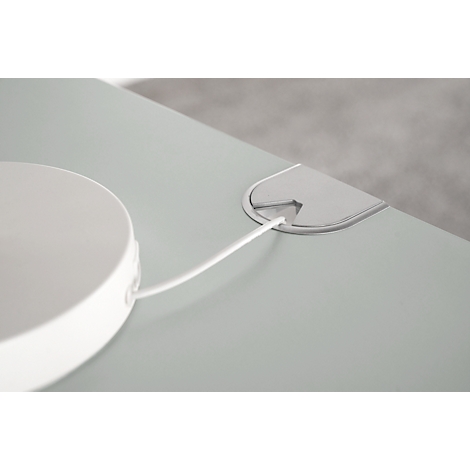 Close-up: White round object with cable leading through a table opening.