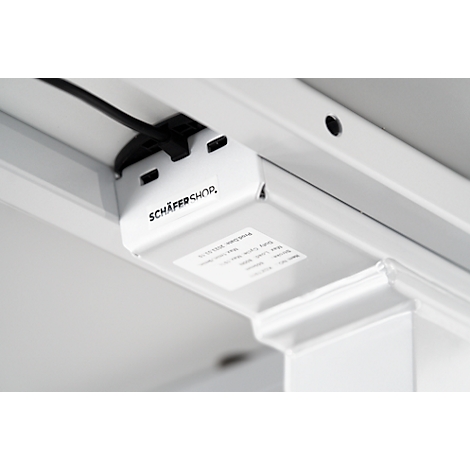 Close-up of the underside of a white desk. A black cable leads to a white connector printed with "SCHÄFER SHOP".