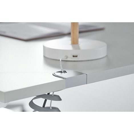 Close-up of a grey desk with an integrated power outlet and cable holder.