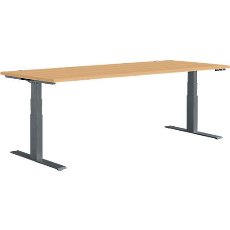 A light-colored, rectangular desk with gray, height-adjustable legs. The tabletop is light brown with a wood grain.