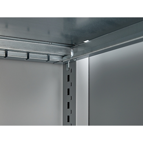 Corner of a metal shelf construction. Gray-silver angles and struts, some with hooks. Light wall in the background.