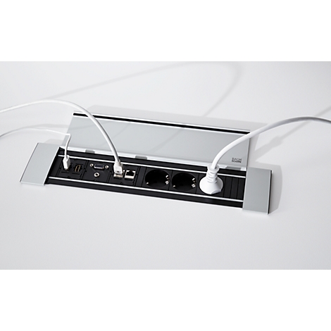 Una conexión de mesa gris con enchufes y conectores. Hay cables blancos enchufados. La tapa está ligeramente abierta.