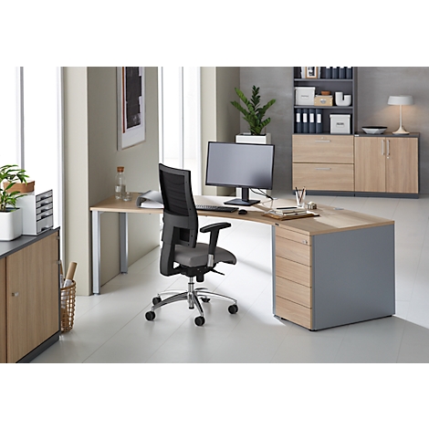 A modern corner desk with office chair in a bright office. On the desk are a monitor, plants and office supplies.