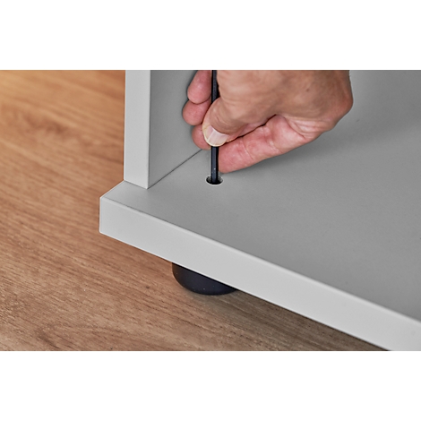 Hand with Allen wrench is screwing a screw into a piece of furniture.