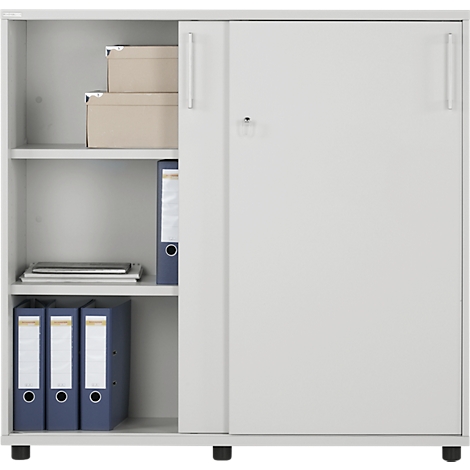 Gray filing cabinet with sliding door. On the left are compartments filled with folders and boxes. The cabinet stands on small black feet.