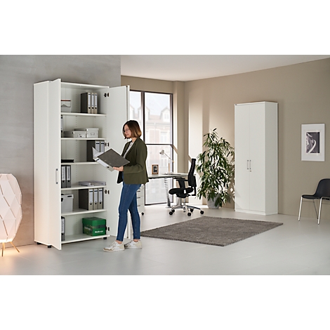 Woman standing in front of a white filing cabinet with open doors, holding a folder. Office with desk, plant, and another cabinet.