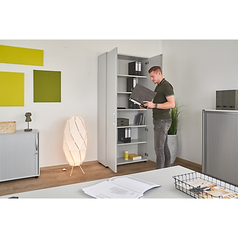 A man stands at an open grey filing cabinet, looking at a folder.