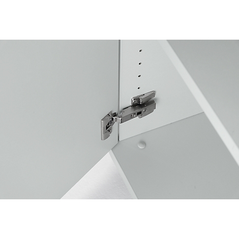 Close-up of a metallic hinge attached to a white cabinet door. Other cabinet parts are visible in the background.