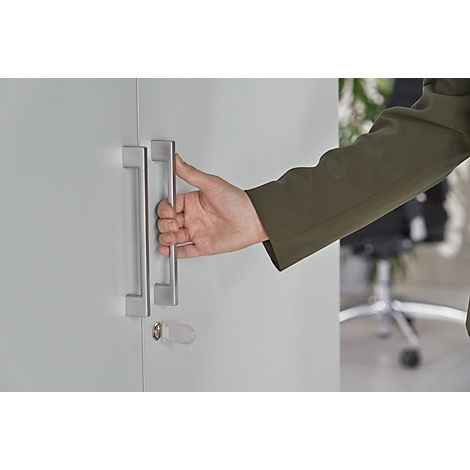 Person opening a cabinet. Hand reaching for the handle, grey cabinet, green jacket.