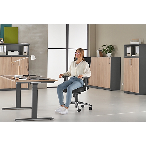 Young woman sitting on an office chair at a desk. Cabinets can be seen in the background.