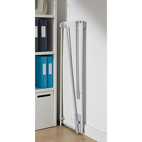 A white foldable wall table with silver legs, leaning against a white wall next to a bookshelf.