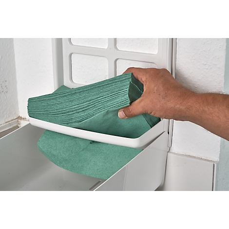 A man's hand removes green wipes from a white dispenser. The wipes are stacked on a white shelf.