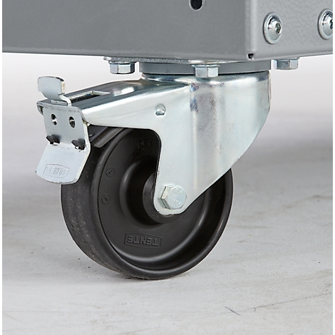 Nahaufnahme eines Rollens an einem grauen Metallgestell. Das Rad ist schwarz, das Gehäuse silbern, mit Feststellhebel.