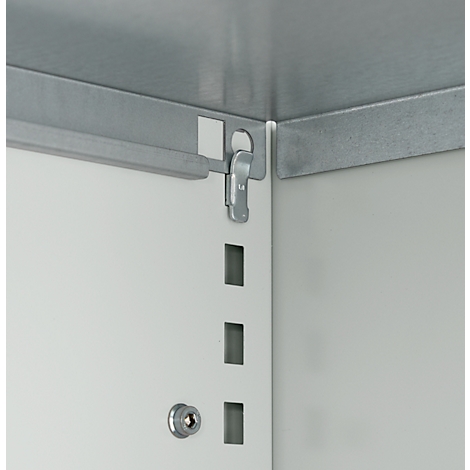 Close-up van een hoek van een kast met een zilveren metalen sluiting die aan een wit oppervlak is bevestigd.