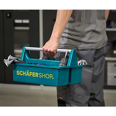 Person trägt eine grüne Werkzeugkiste mit dem Schriftzug SCHÄFER SHOP; Werkzeug liegt darin.