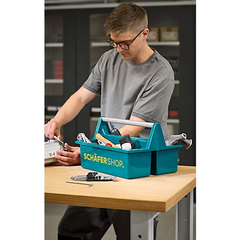 Mann mit Brille arbeitet an Tisch. Vor ihm blaue Werkzeugkiste mit Werkzeug, Aufdruck: Schäfershop.