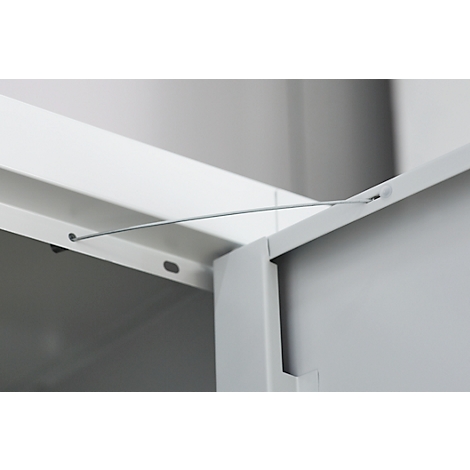Detail of a cabinet corner joint. A wire spans between two white metal parts.