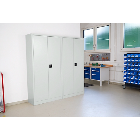 Two gray cabinets with black handles stand in front of a white wall. Tools and windows in the background.