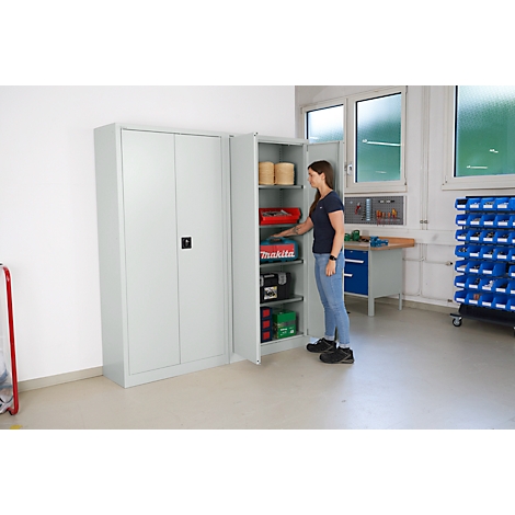 A woman stands by an open tool cabinet. Tools and materials are stored in the cabinet.