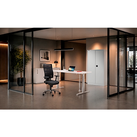 Modernes Büro-Interieur mit höhenverstellbarem Schreibtisch, schwarzem Drehstuhl und einem weißen Metallschrank.
