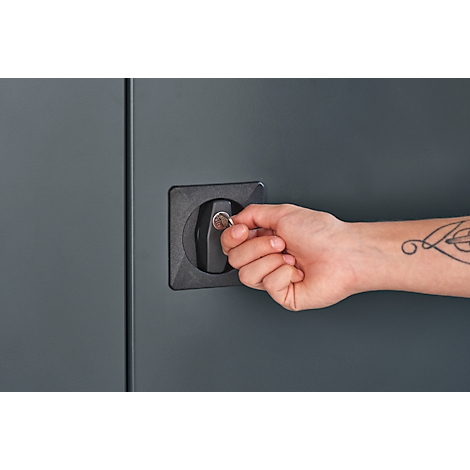 Gros plan: Personne ouvrant une porte d'armoire verrouillée. La main insère la clé dans la serrure. Il y a un tatouage sur le bras.