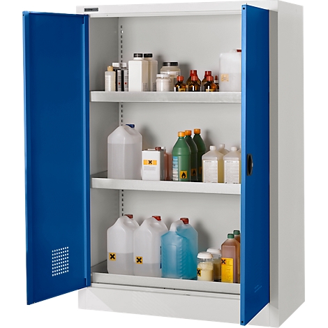 Armoire blanche ouverte avec portes bleues, remplie de divers produits chimiques dans des bouteilles et des conteneurs. Des panneaux d'avertissement jaunes et oranges sont visibles.
