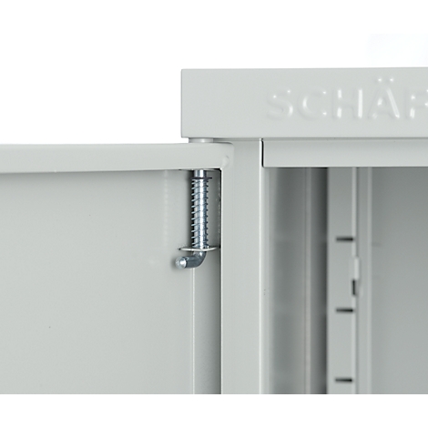 Gros plan d'une armoire grise avec charnière de porte ouverte et ressort. En haut, il est écrit « SCHÄ… » en lettres en relief.
