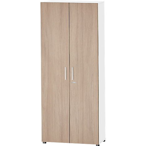 Une grande armoire à deux portes en bois brun clair. Les côtés sont blancs, elle a deux poignées argentées et une serrure.