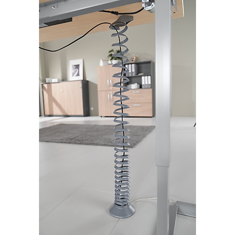 Grijze kabelspiraal onder het bureau, detailopname. Het bureau is licht, kasten erachter.