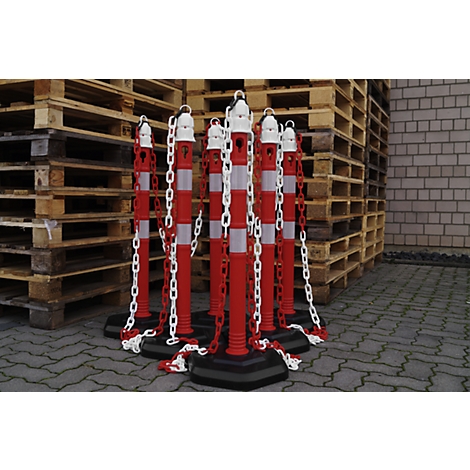 Red and white striped bollards with white chains. In the background pallets and a brick wall.