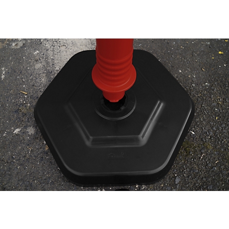 Black hexagonal base of a red-orange marker post, on a grey surface.