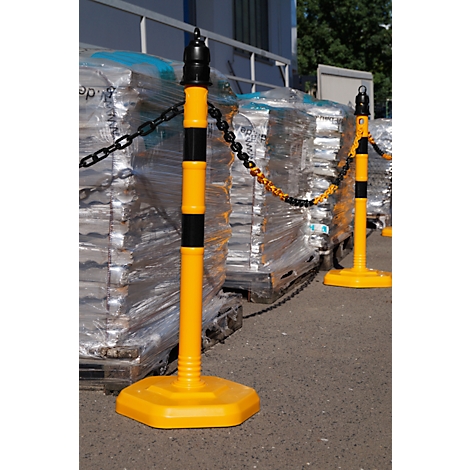 Yellow and black bollards with chain blocking off area. In the background pallets with goods.