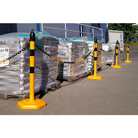 Yellow and black barrier posts with chain in front of stacks of goods on pallets.