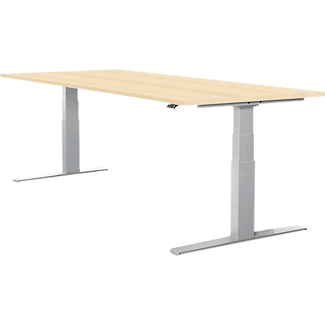 A height-adjustable desk in light wood with silver legs. The tabletop is rectangular, the legs have a T-shaped design.