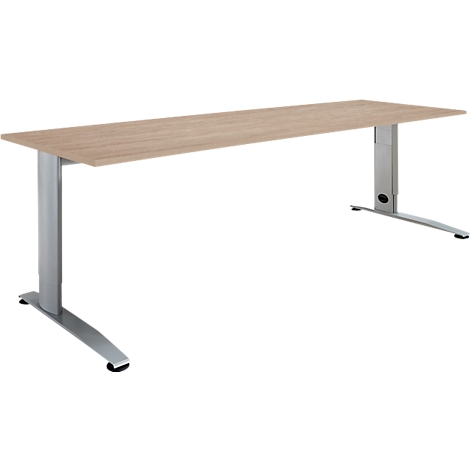 Desk with wooden top and silver, height-adjustable legs. One leg is on the left, one on the right.