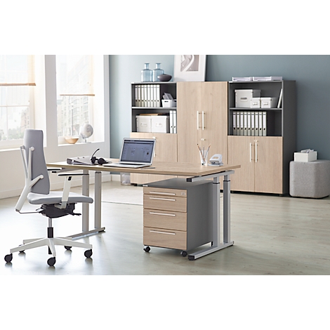 An office with a height-adjustable desk, swivel chair, and wall unit. A laptop and headset sit on the table.