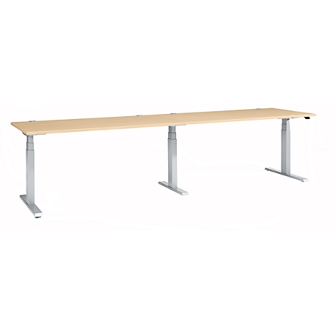 A long, height-adjustable desk with a light wood top and silver legs.
