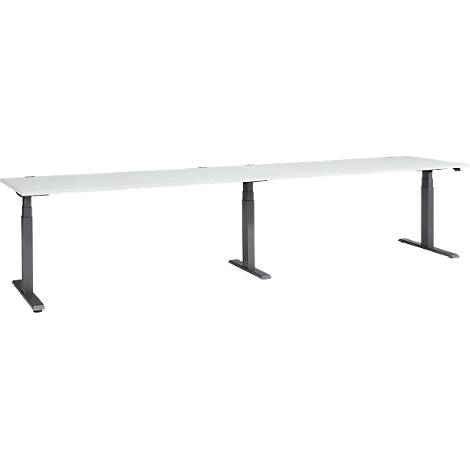 A long, white desk with three dark, height-adjustable legs, in front of a white background.