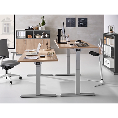 Office with two height-adjustable desks, office chairs, and shelving. Laptops and accessories are on the tables.