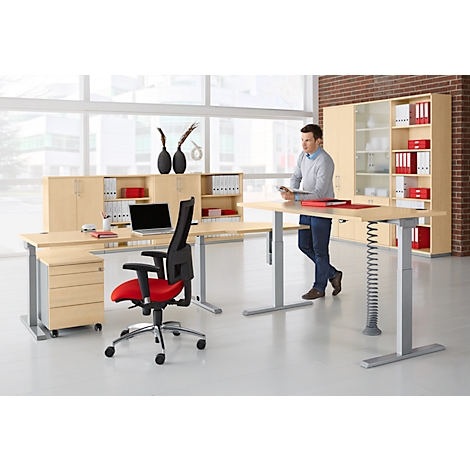 A man at a height-adjustable desk. Office furniture in the background, desk chair with a red seat.