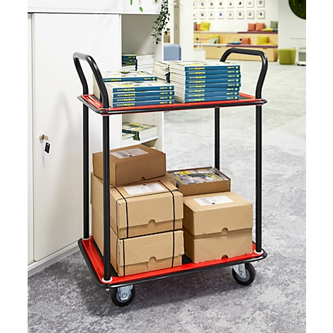 Ein roter Servierwagen mit Büchern und Paketen in einem Büro. Auf der obersten Ebene liegen Bücher, darunter Kartons. Schwarzer Griff.