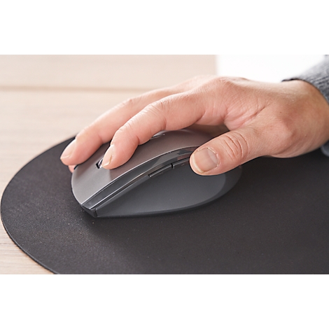 Eine Hand greift eine graue Computermaus, die auf einer schwarzen runden Unterlage liegt.