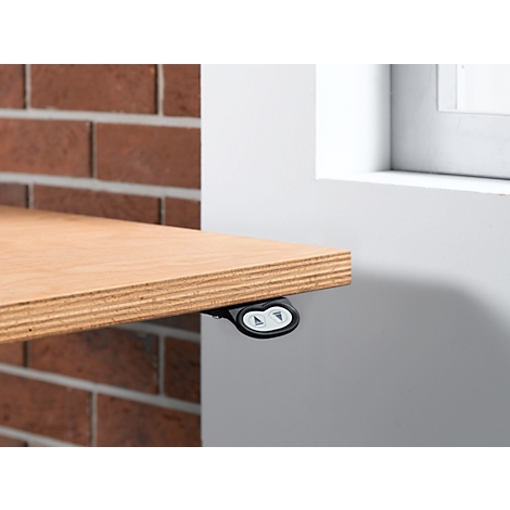 Close-up of a table top with control panel for height adjustment. The table is attached to a brick wall and a white wall.