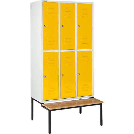 Een witte locker met gele deuren en een houten bank ervoor.