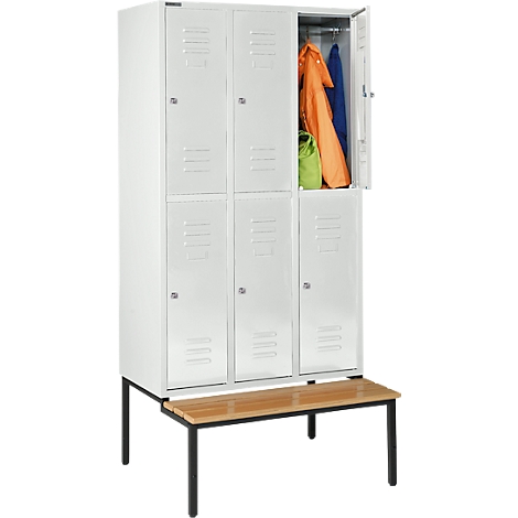 Witte kluis met open deur met kleding. Daaronder een houten bank met zwarte poten.