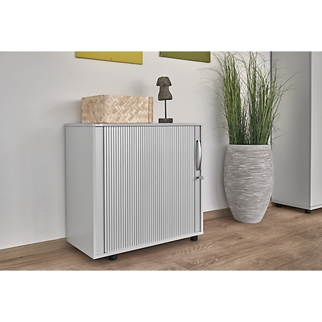 Grey cabinet with ribbed front and decor on top. To the right, a tall vase with ornamental grass.